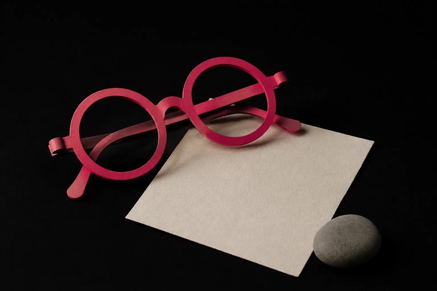 Rose paper spectacles resting beside a plain grey card.