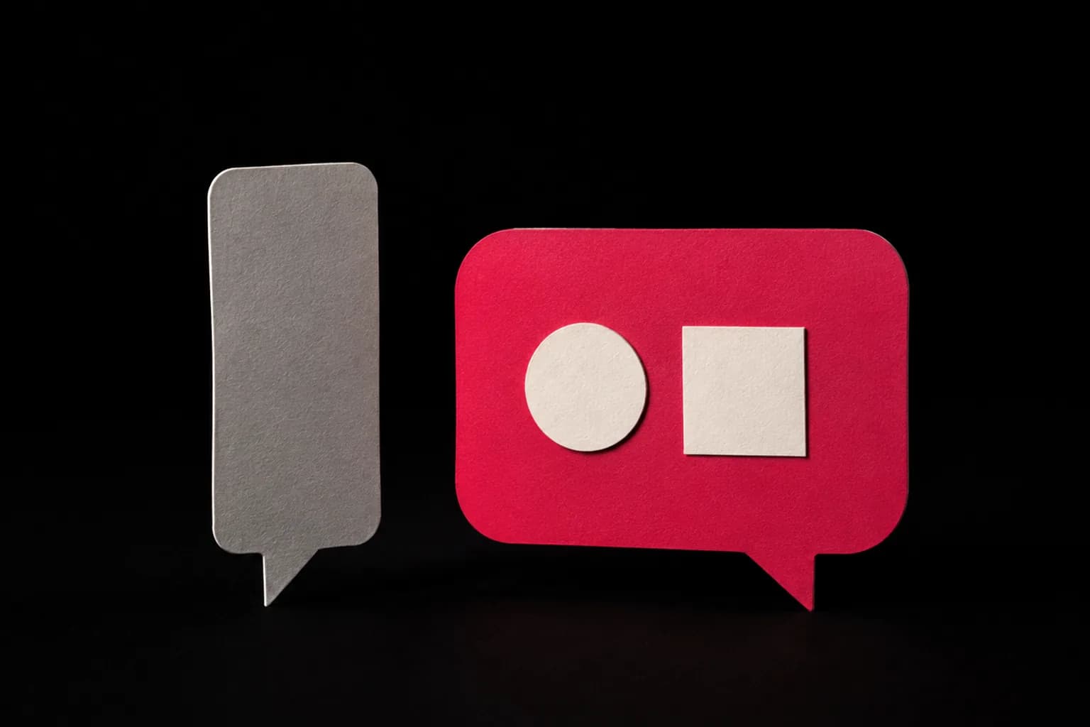 A plain narrow paper speech bubble beside a wider bubble holding two small paper shapes.